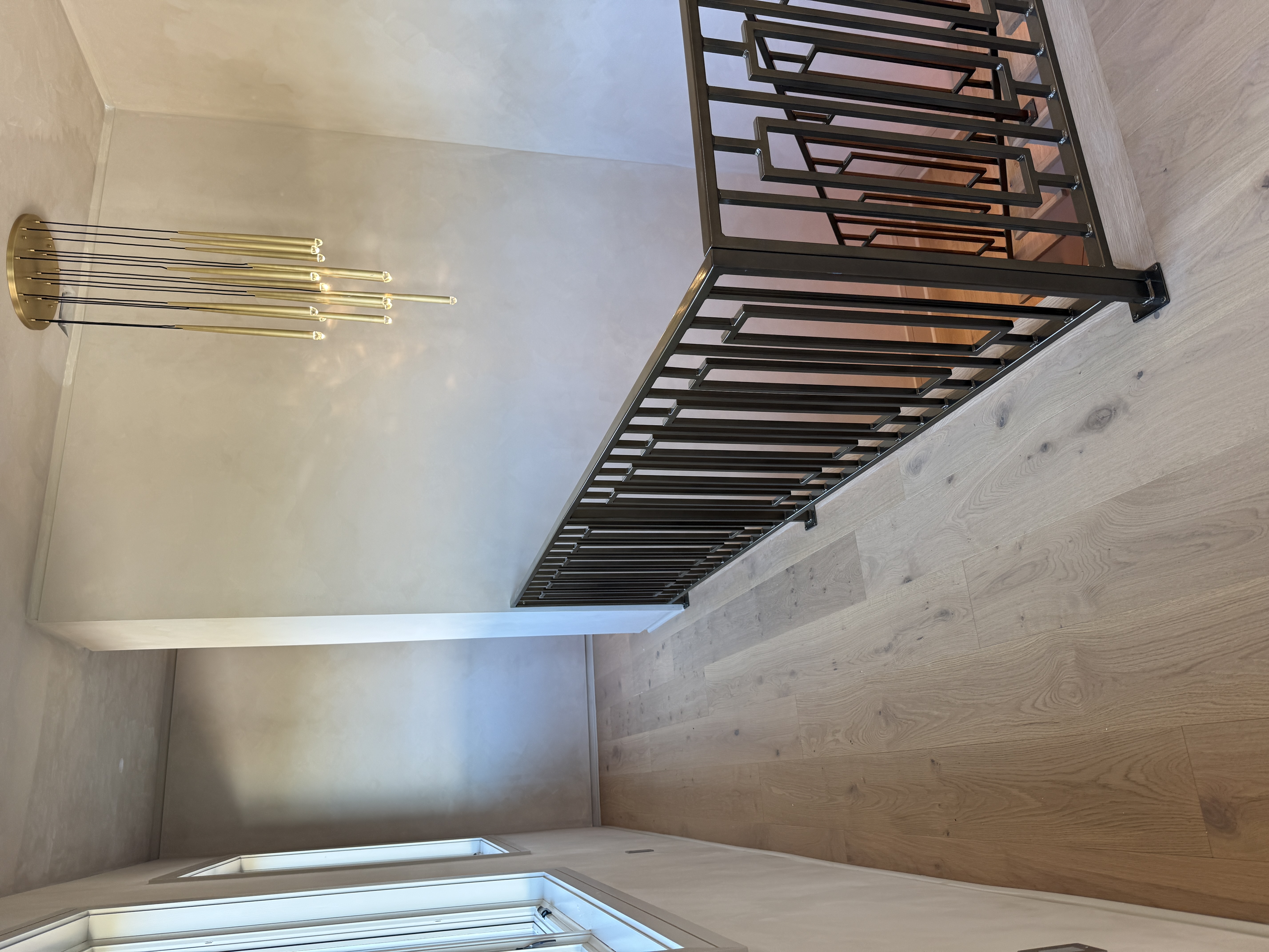 Interior stair landing with a blackened-steel railing, hardwood floor, and plaster wall