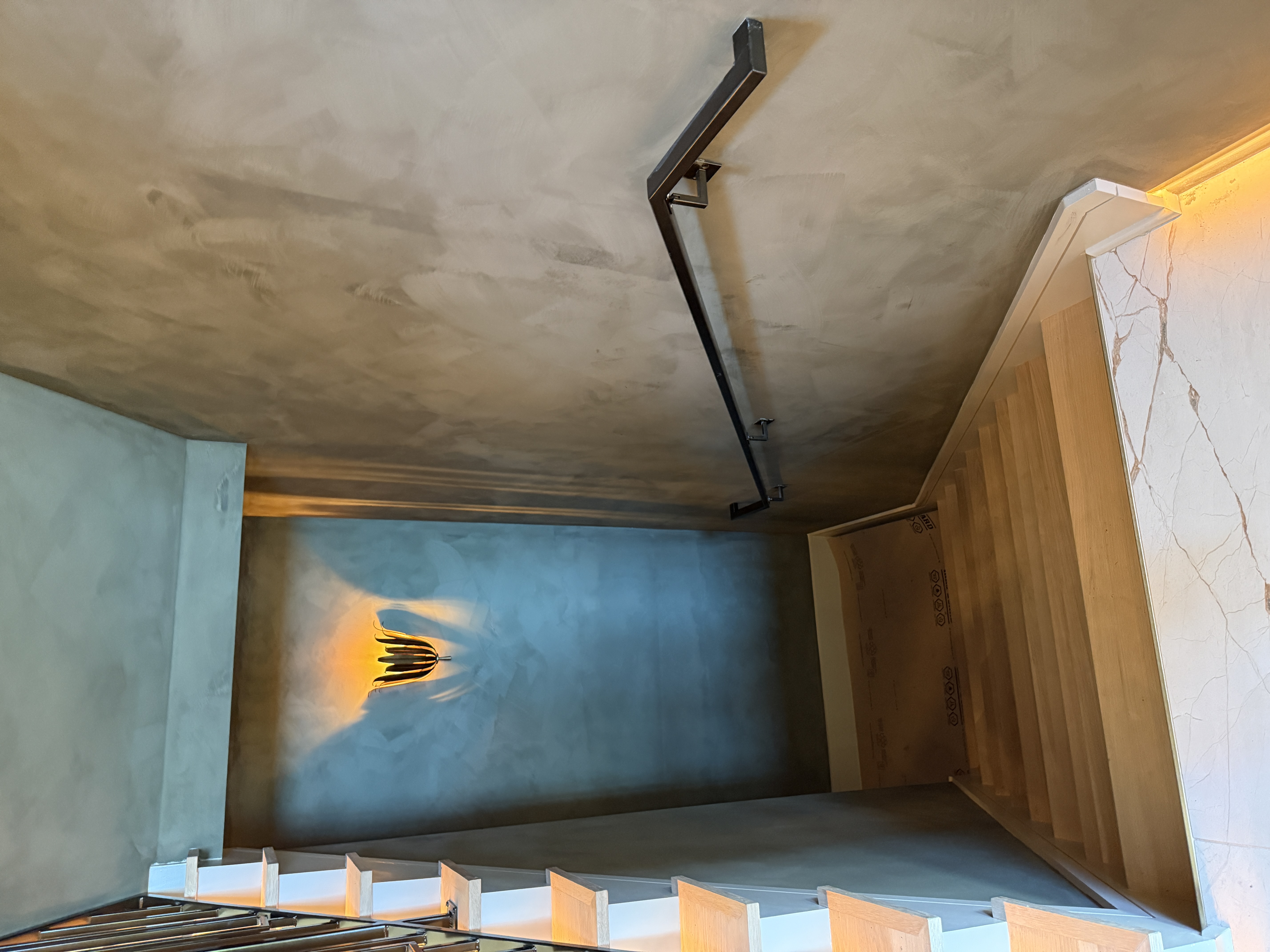 Interior stair with a blackened-steel handrail on a plaster wall