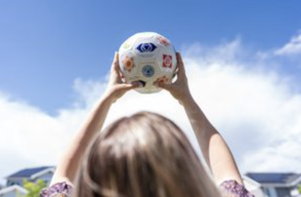 A person holding a ball up toward a bright blue sky