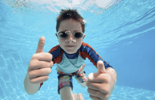 A young boy giving two thumbs up underwater in a pool