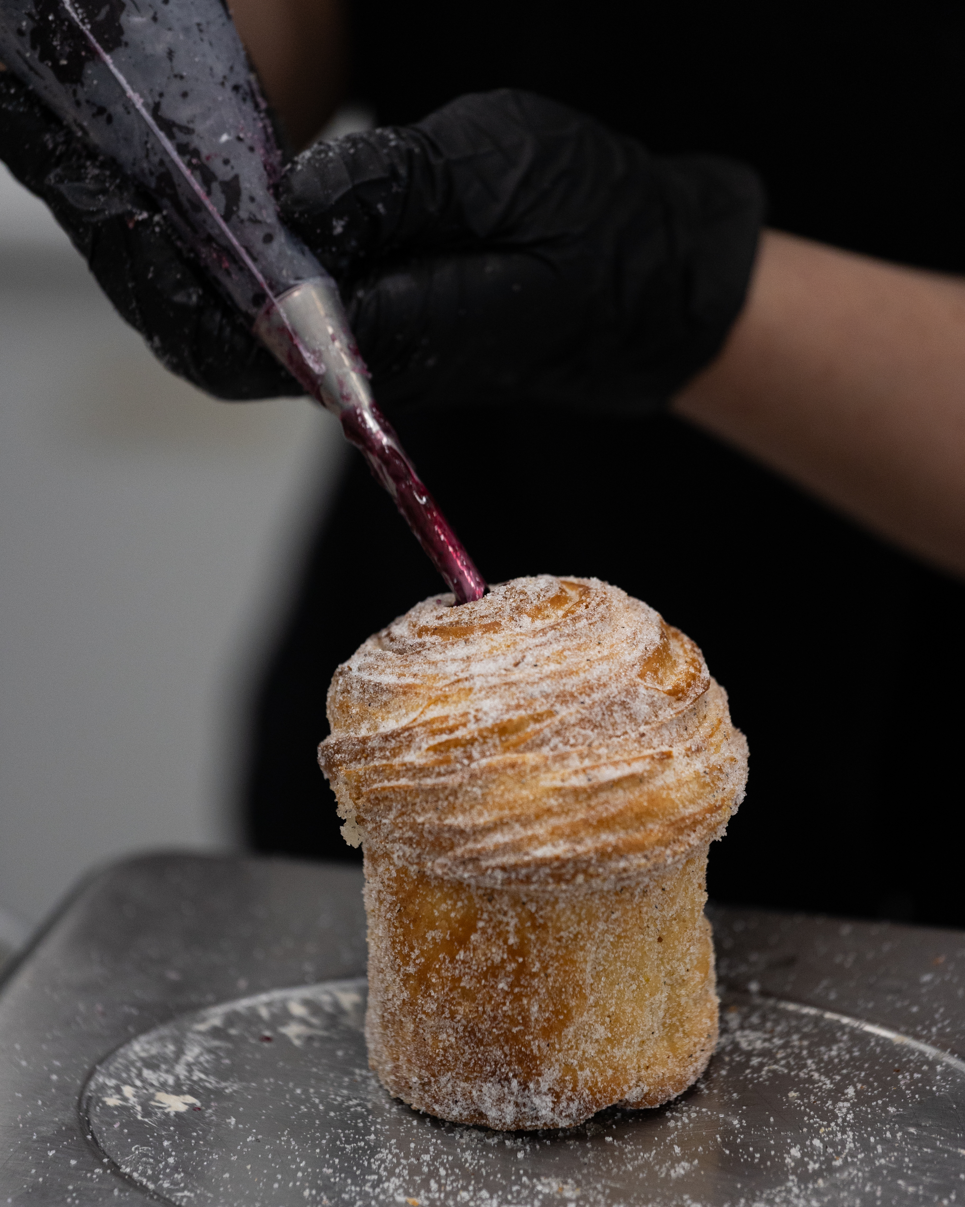 A baker piping berry filling into a sugar-coated cruffin
