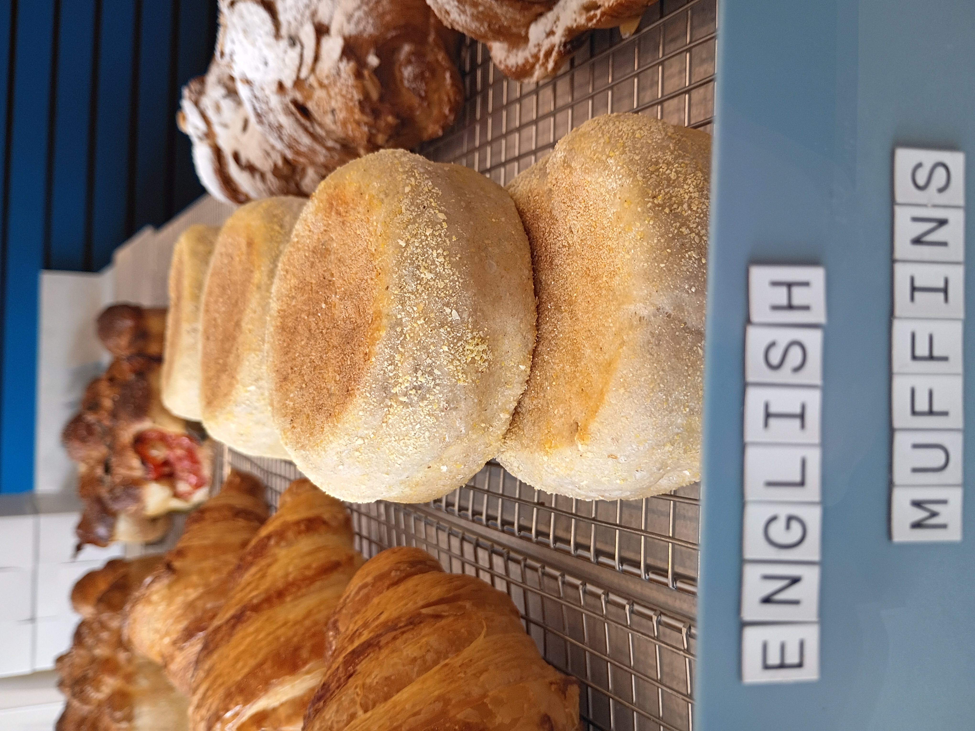 Fresh English muffins dusted with cornmeal alongside golden croissants on a cooling rack