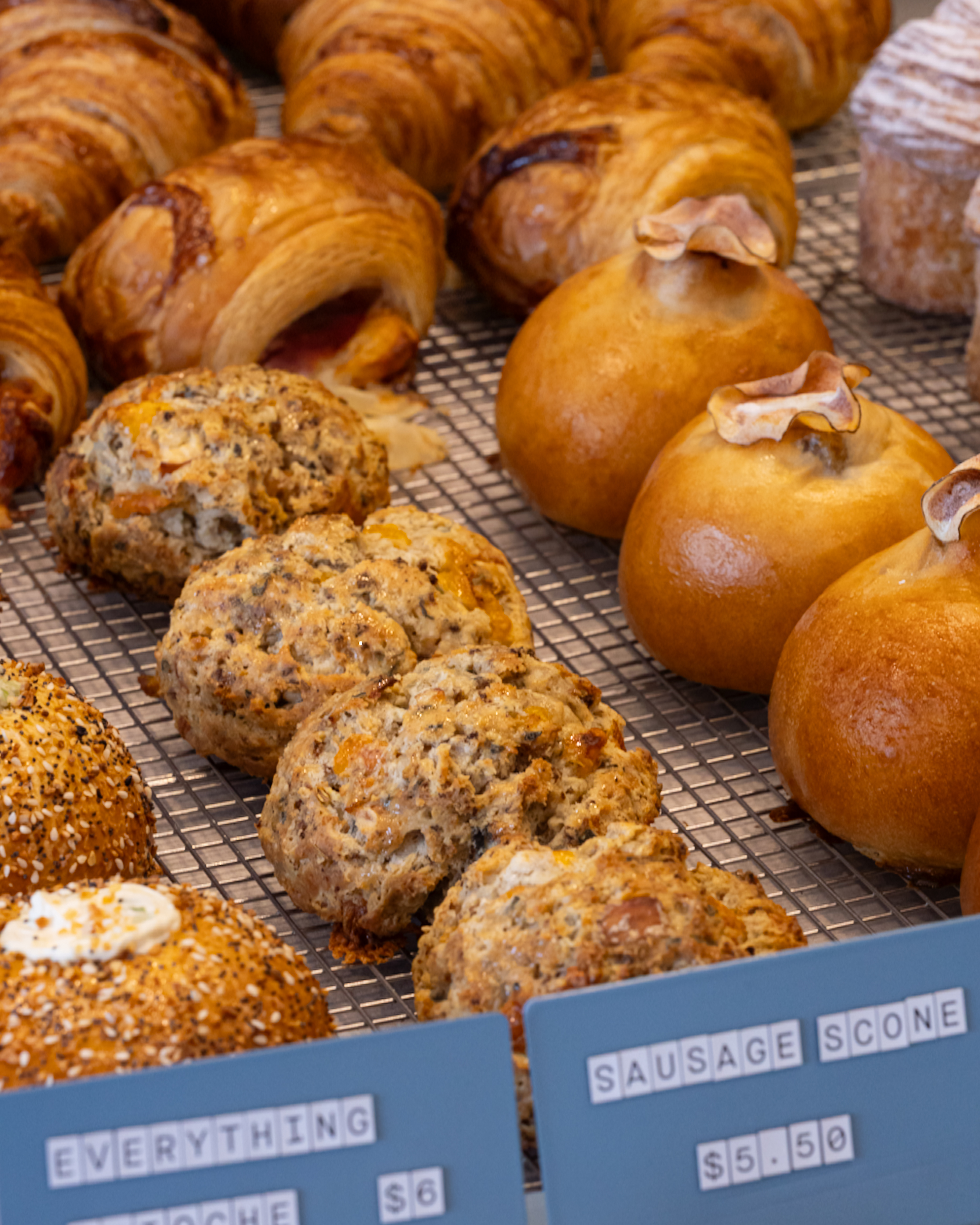 An assortment of fresh croissants, brioche, and scones on a cooling rack at Back Roads Bread Co